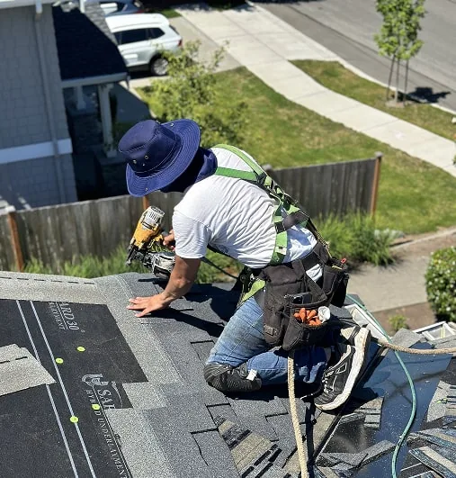 Roofer fastening shingles along a roof edge